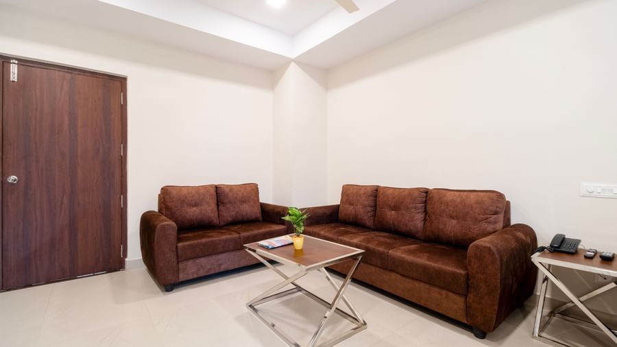 Modern lounge area with brown sofas, glass table and simple decor for relaxation at Swarna's The Capital.