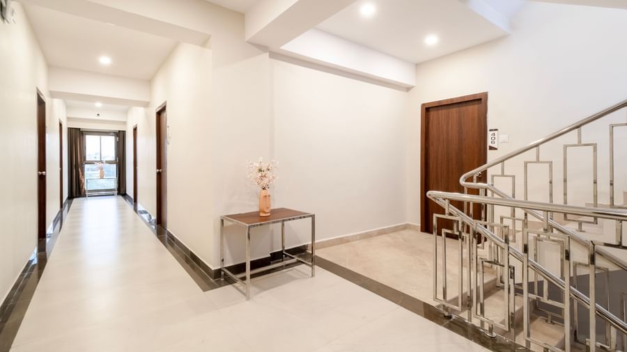 Bright hotel corridor with white walls polished flooring and modern staircase at Swarna's The Capital.