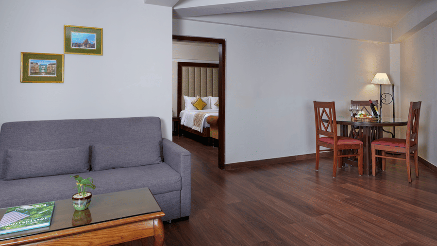 The Family Suite bathroom at Swosti Premium, Bhubaneswar,  with a sofa, tables, chairs, and a bed visible in the room.
