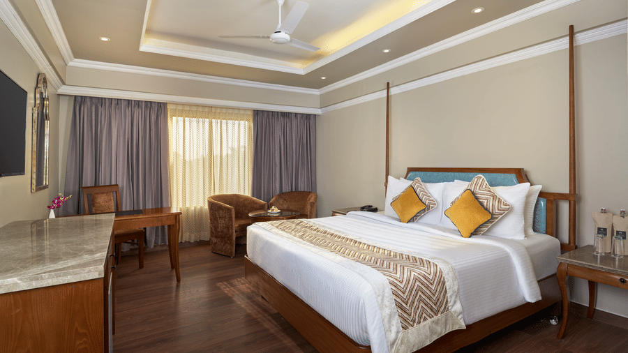 The Premium King Room at Swosti Premium, Bhubaneswar, featuring a double bed, bedspreads, pillows, chairs, tables, and a television.