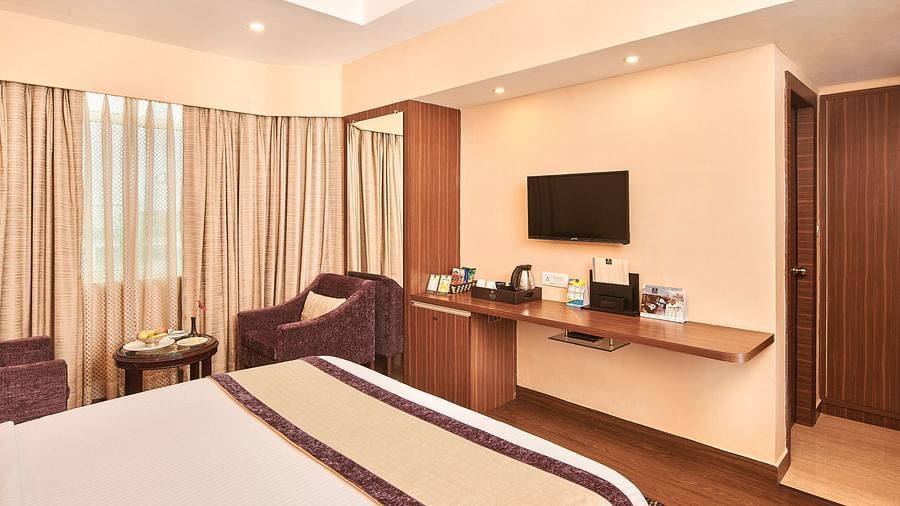 Deluxe Room with bed and a television in front of it and large window on the side at Swosti Grand, Bhubaneswar