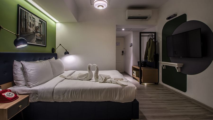 A well-lit hotel room with a king size bed, two bedside tables, TV, and a large mirror. The room is decorated with artwork and stylish lamps  | T24 Retro