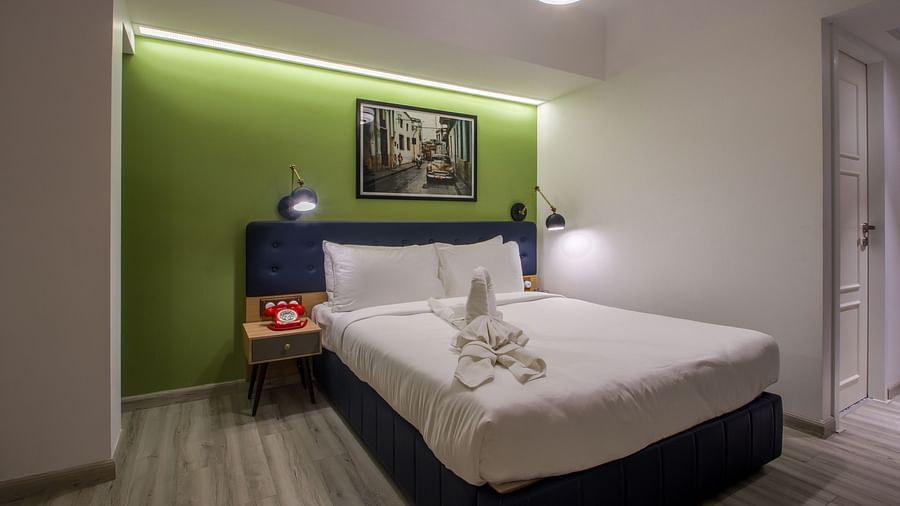 A modern and colorful hotel room with a comfortable bed and a vibrant green accent wall  | T24 Retro