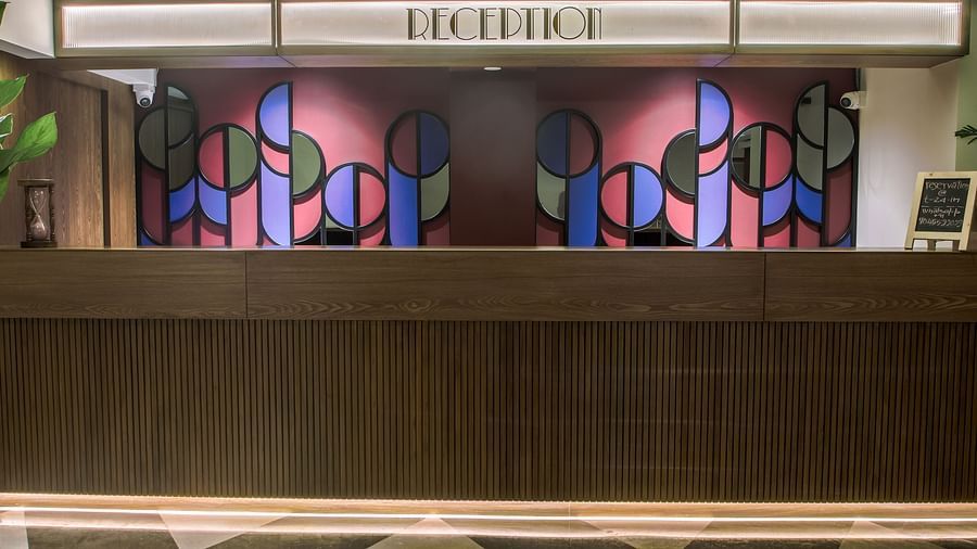 The reception desk at T24 Retro Hotel , with a colourful geometric design behind it  | T24 Retro