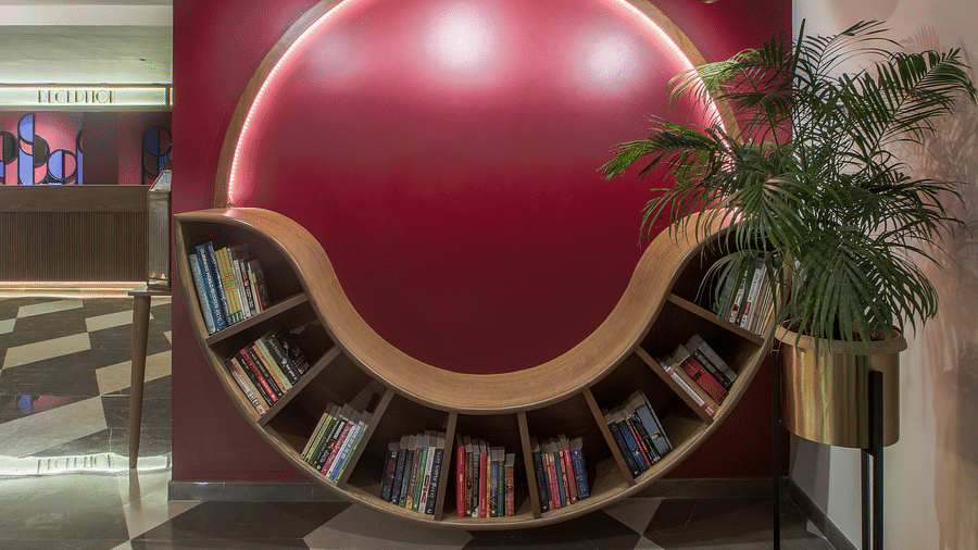 A unique, curved wooden bookshelf with a red wall behind it. The bookshelf is shaped like a wave and is filled with books.