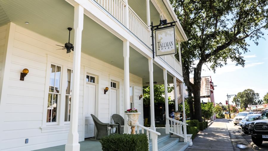 A side view of the charming Tallman Hotel shows its inviting porch, white facade, and a sign hanging over the entrance.