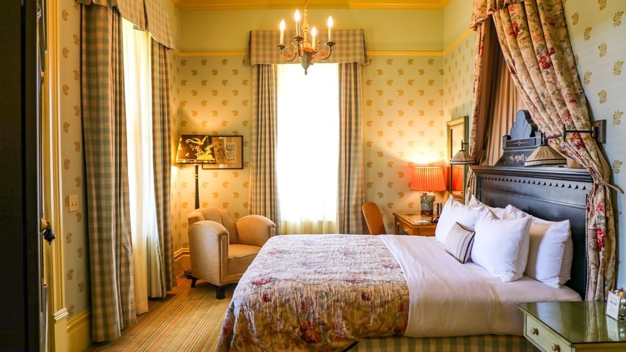 A luxurious and elegantly decorated bedroom at the Tallman Hotel, featuring a four-poster bed and chandelier.