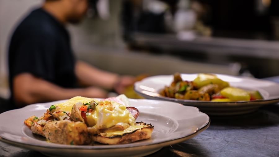 Freshly prepared gourmet dishes sit on a counter with a chef in the background at the Tallman Hotel.