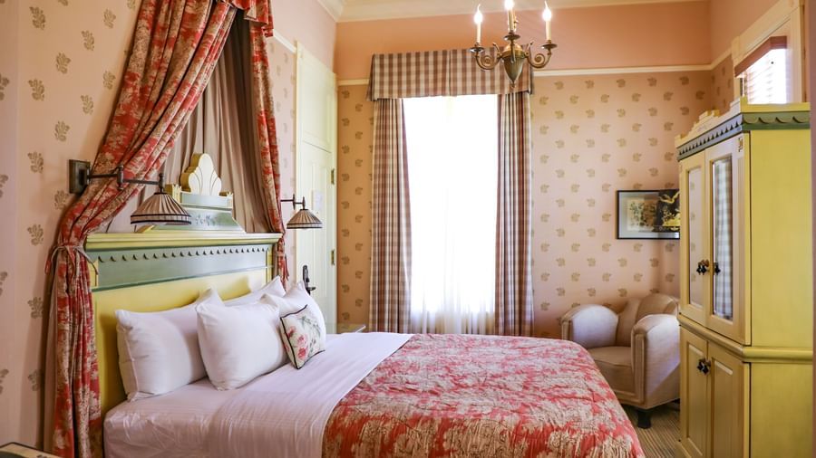 A charming Tallman Hotel room offers a cozy bed with decorative drapes and a vibrant red and white patterned bedspread.