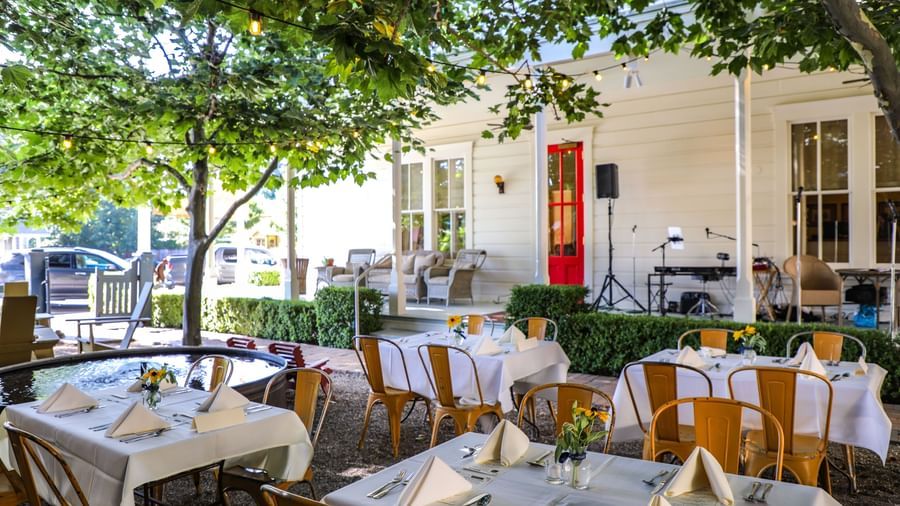 A Garden Veranda with multiple dining tables and chairs with trees at Tallman Hotel.