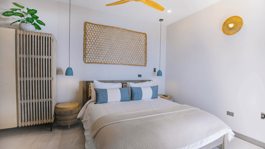 A bedroom with a king size bed, a cupboard, a ceiling fan, plants, and lighting at Tamarind Hills Resort and Villas, Antigua.