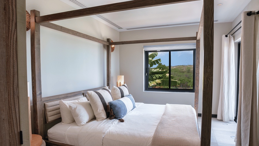 A bed with bedside tables and a large window overlooking the sea in Suite 35 at Tamarind Hills Resort and Villas.