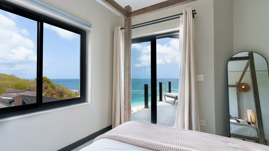 A bedroom with a bed positioned beside large windows overlooking the sea in Suite 35 at Tamarind Hills Resort and Villas.