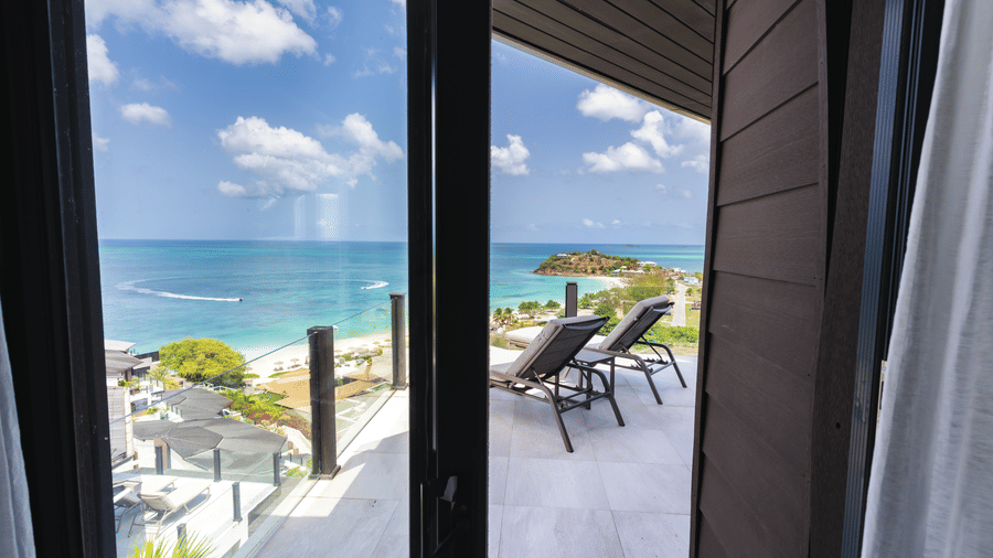 A view through the glass doors towards the private deck, swimming pool, sun loungers, and sea beyond at Suite 35, Tamarind Hills Resort and Villas.
