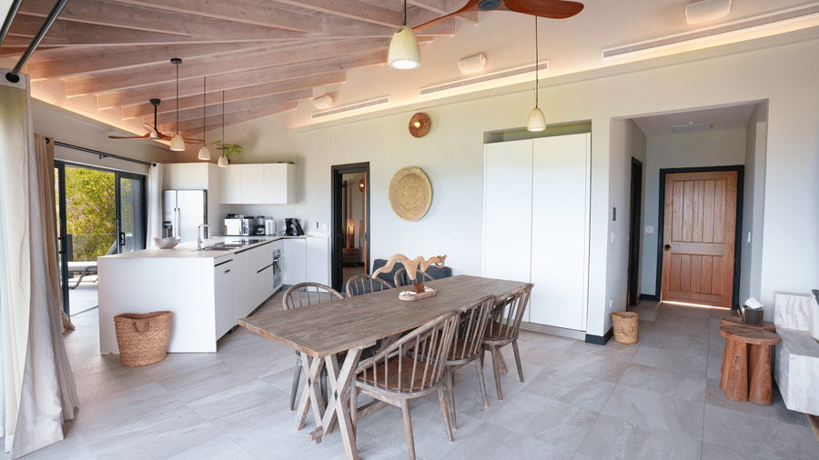 An open-plan dining and kitchen area with a dining table, chairs, kitchen counter, ceiling fans, and glass doors in Suite 35 at Tamarind Hills Resort and Villas.