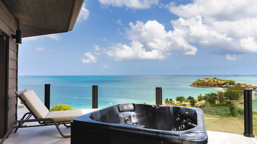 A private deck with a jacuzzi and sun loungers overlooking the swimming pool, coastline, and sea at Suite 35, Tamarind Hills Resort and Villas.