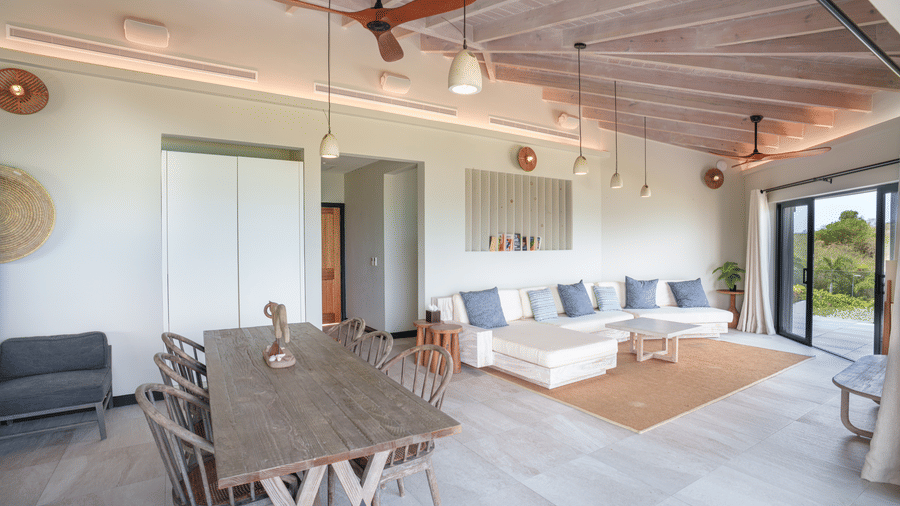 An open-plan living and dining area with a dining table, chairs, sofas, ceiling fans, and large glass doors in Suite 35 at Tamarind Hills Resort and Villas.