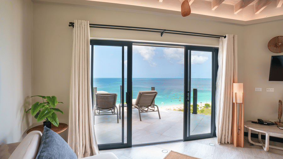 A living area with a sofa, floor lamp, ceiling fan, and large glass doors opening towards the terrace and sea in Suite 35 at Tamarind Hills Resort and Villas.