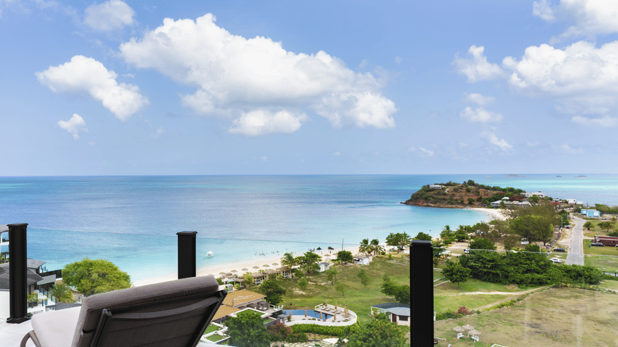 A sea-facing terrace with an outdoor chair overlooking the swimming pool, landscaped grounds, coastline, and open sea at Suite 35, Tamarind Hills Resort and Villas.