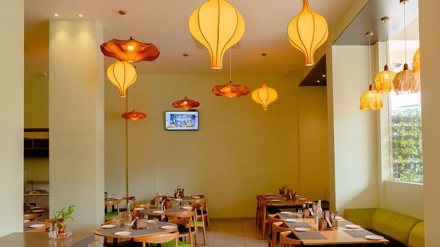 An empty restaurant interior with tables set for dining and hanging orange pendant lights - TGI Ameya Grand, Goa