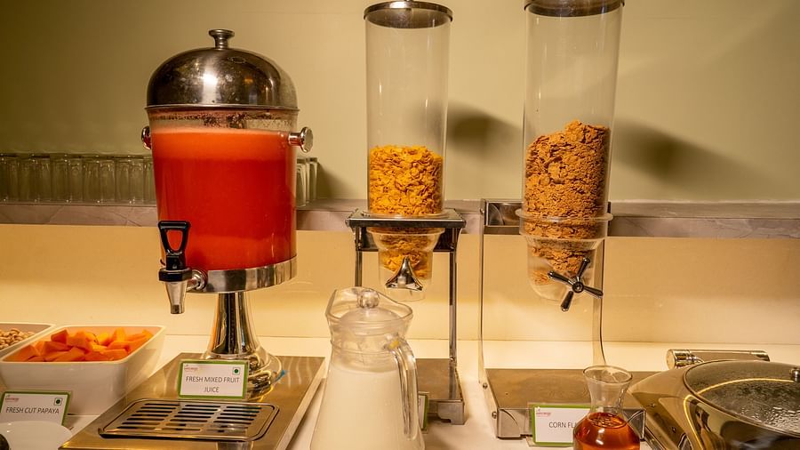 A buffet selection featuring fresh mixed fruit juice in a dispenser and cereals in clear containers - TGI Ameya Grand, Goa