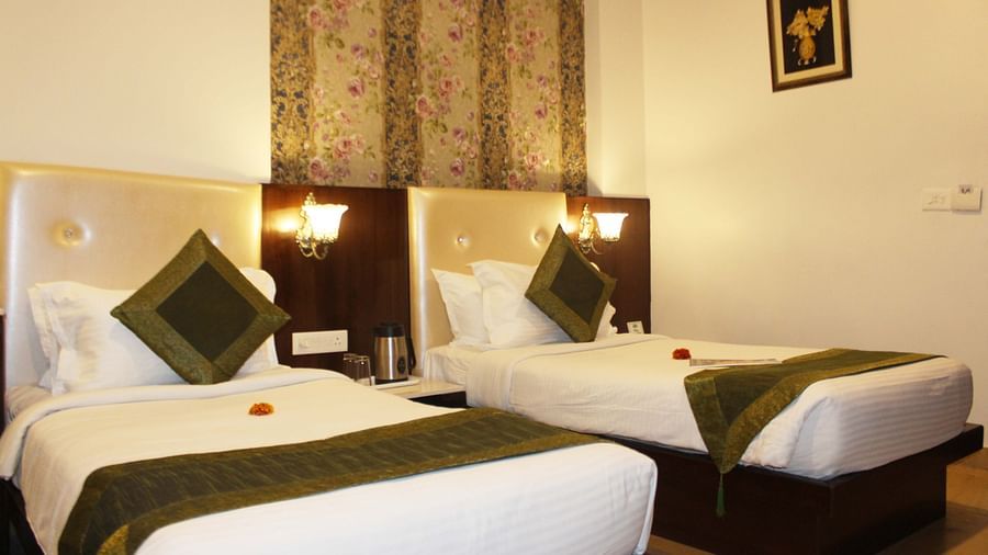 A hotel room with two beds, green runners, floral wallpaper and a wooden headboard - TGI Apple Inn, Jaipur 
