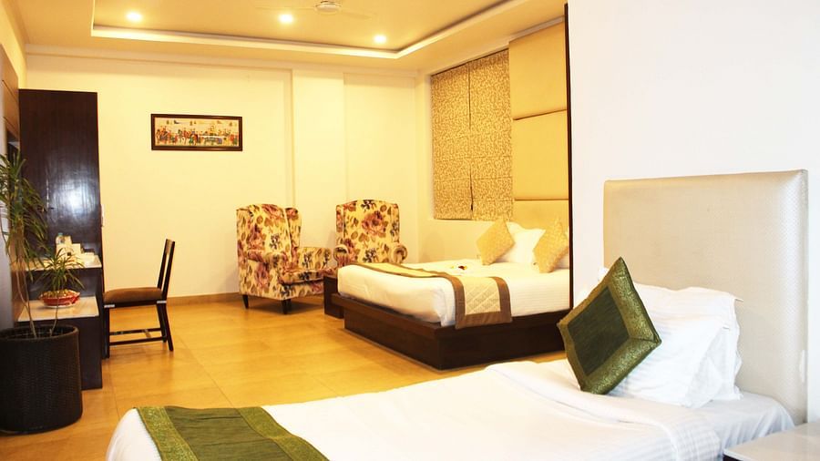 A spacious hotel room with two armchairs, a large bed with white linens and patterned wallpaper - TGI Apple Inn, Jaipur 