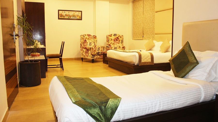 Another view of a spacious hotel room with two armchairs, a large bed with white linens and patterned wallpaper - TGI Apple Inn, Jaipur 