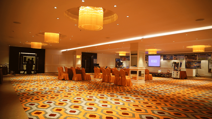 A banquet hall with orange chair covers and a central projection screen, under warm yellow lighting - TGI Grand Fortuna, Hosur