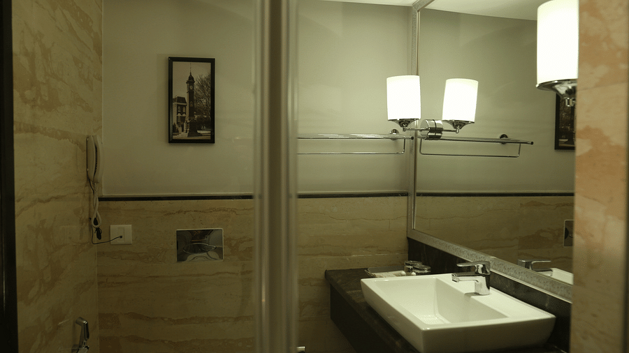 A bathroom interior with modern amenities featuring a large mirror above a white rectangular sink - TGI Grand Fortuna, Hosur