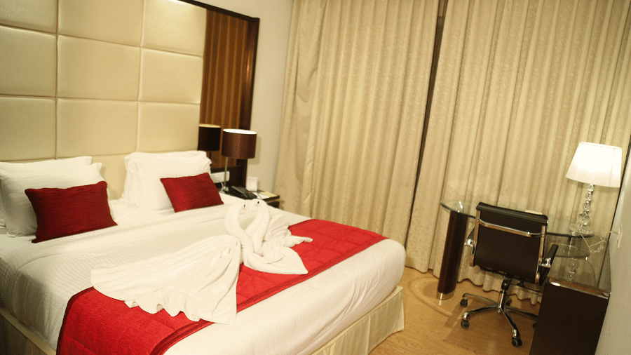 A hotel room with a king bed with red throw, white linens and towel art - TGI Grand Fortuna, Hosur