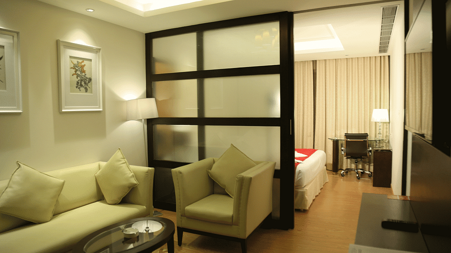 Hotel suite with cream sofa, armchairs and room divider leading to the bed - TGI Grand Fortuna, Hosur