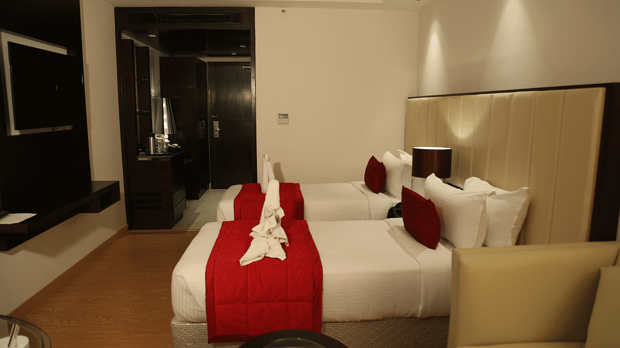 A hotel room viewed from a different angle showing two twin beds with red bedspreads and a padded headboard - TGI Grand Fortuna, Hosur