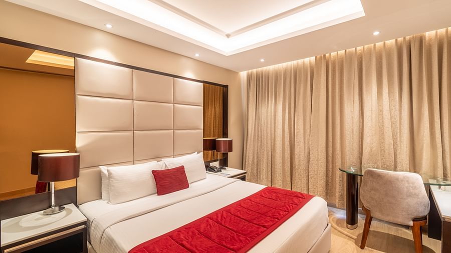 Fortuna suite's bedroom with full-length curtains, bedside table, and armchair- TGI Grand Fortuna, Krishnagiri Main Road, Hosur