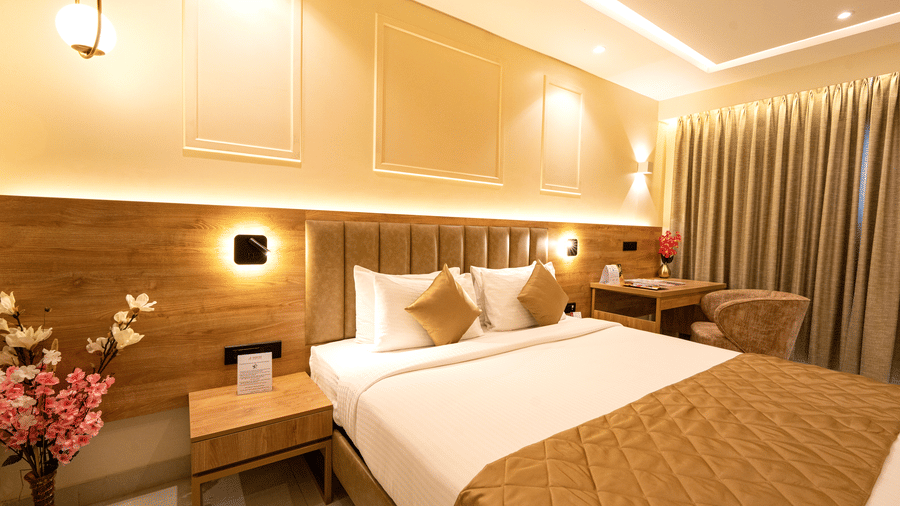 Well lit bedroom with a king bed, side table, flower vase with pink flowers and curtained windows at TGI Star Holiday Resort.