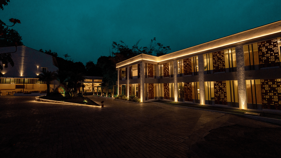    Alt Text: Night view of TGI Star Holiday Resort on Salem Main Road, Yercaud, featuring modern two?story buildings with large windows, decorative wall patterns, warm lighting, surrounding trees, and a paved courtyard creating an elegant atmosphere.