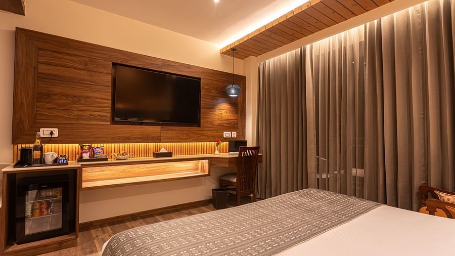 An image of a Deluxe room with a bed, flat screen TV, a fridge, and subtle lighting for decoration - The Belvedere Himalayan Retreat, McLeodganj