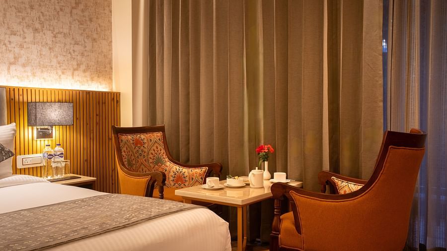 An image of a Deluxe Room with a bed, bed side table, lamps, and chairs and table - The Belvedere Himalayan Retreat, McLeodganj