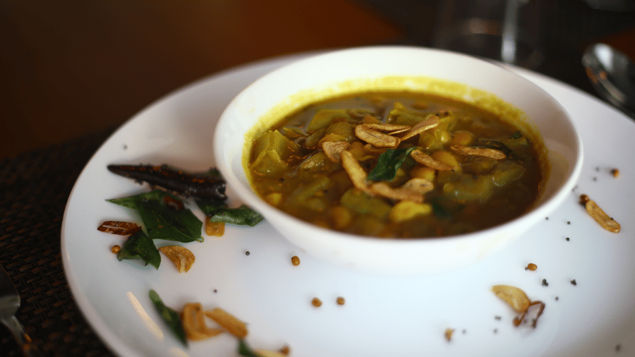 A close-up of a flavourful yellow curry dish served in a white bowl on a dark place mat at The Bull Boutique Hotel.