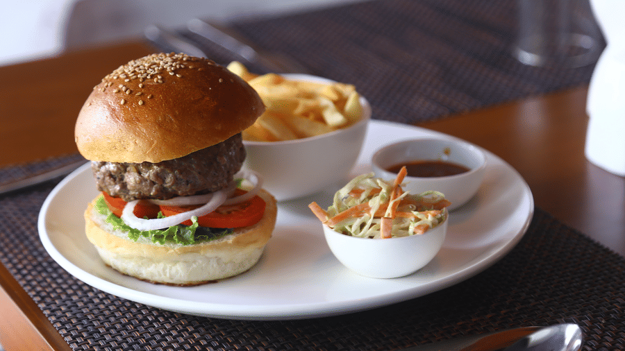 A gourmet beef burger with lettuce and tomato on a toasted bun, served with a side of coleslaw and golden French fries at The Bull Boutique Hotel.