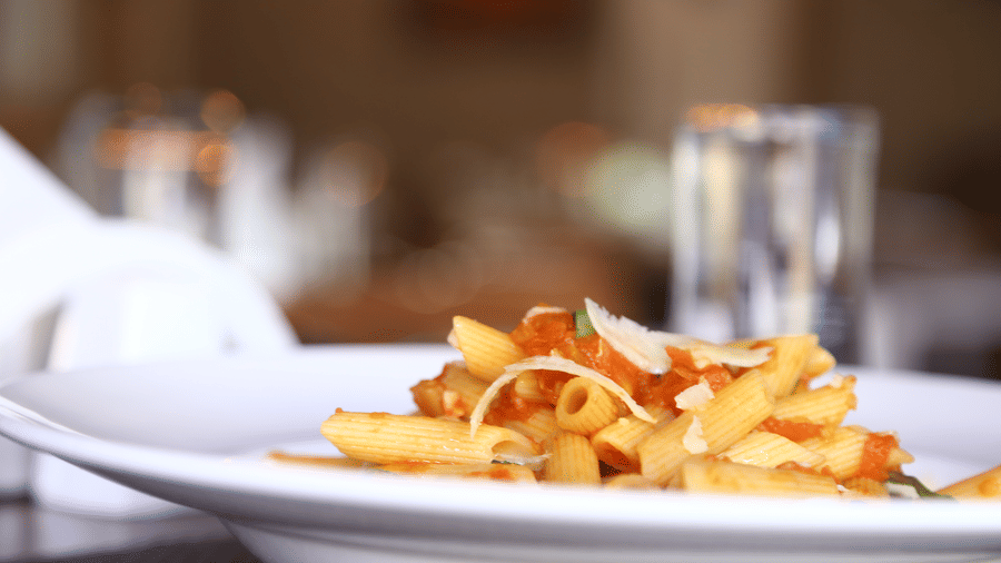 A close-up, side-angle view of a plate of french fries topped with red sauce, fresh herbs, and shaved Parmesan cheese at The Bull Boutique Hotel.