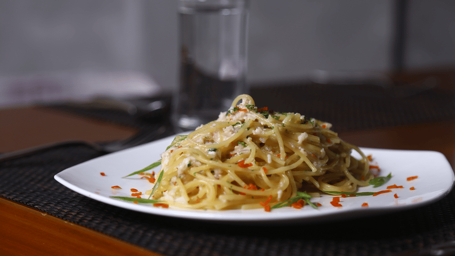A white plate featuring a serving of spaghetti aglio e olio garnished with finely chopped vegetables and herbs at The Bull Boutique Hotel.