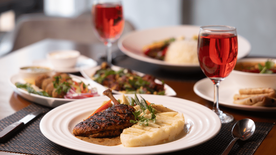 Plated gourmet meals including roasted chicken, mashed potatoes, and glasses of red wine on a restaurant table.
