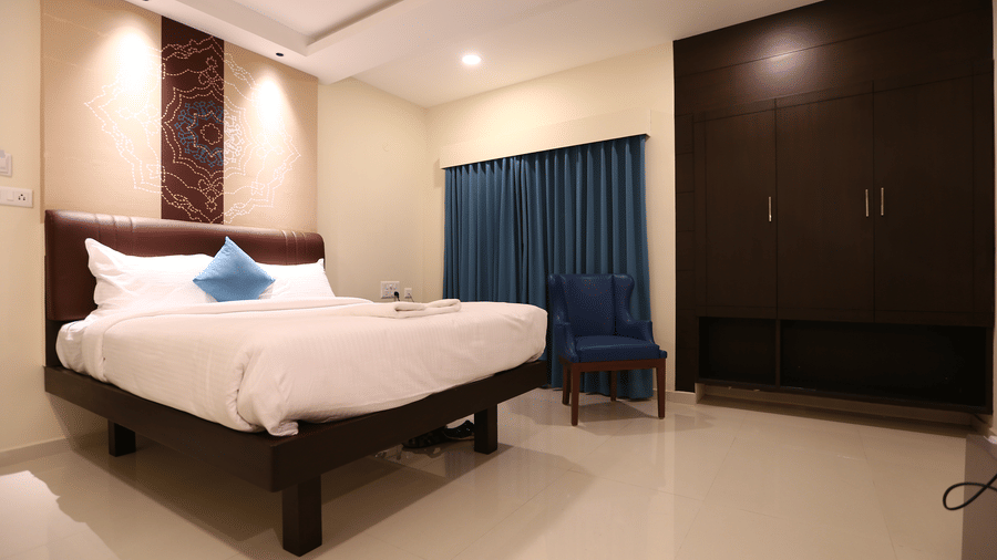 A spacious bedroom featuring a dark wood bed frame, matching large wardrobe, and a blue velvet accent chair at The Bull Boutique Hotel.