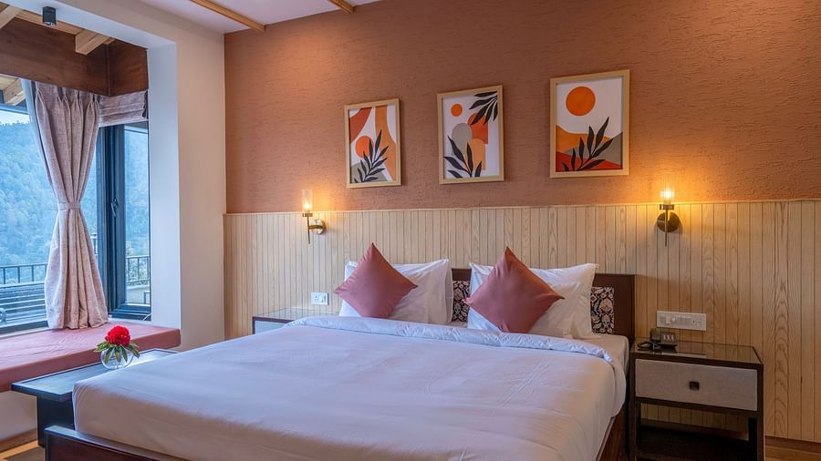 A view from the foot of the bed at The Chamomile Estate, showcasing bedside tables with wall-mounted lamps on either side of the headboard, and a window with curtains drawn aside.
