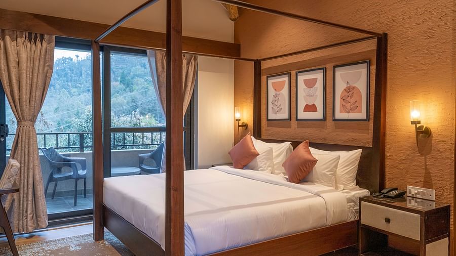 Bedroom with a four-poster bed, bedside table with a wall-mounted light, and a balcony with a view, with curtains pulled to the side at The Chamomile Estate.