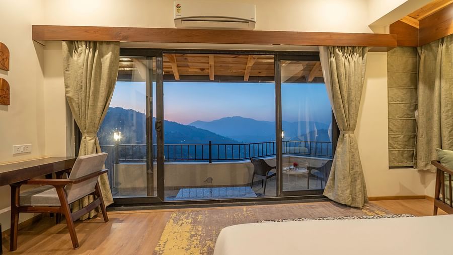 Spacious room with a bed, study desk, and chair beside the balcony overlooking a view at The Chamomile Estate.