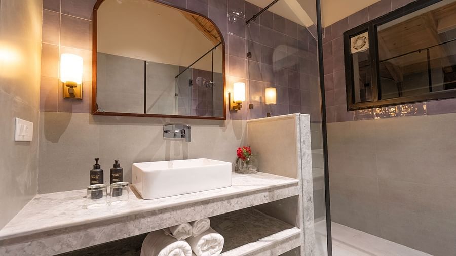 Well-lit bathroom with a sink and a large mirror, essentials placed beside the sink, and rolled towels stored below at The Chamomile Estate.