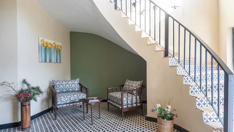 A lobby at The Chamomile Estate featuring cushioned seating and a curved staircase to the side.