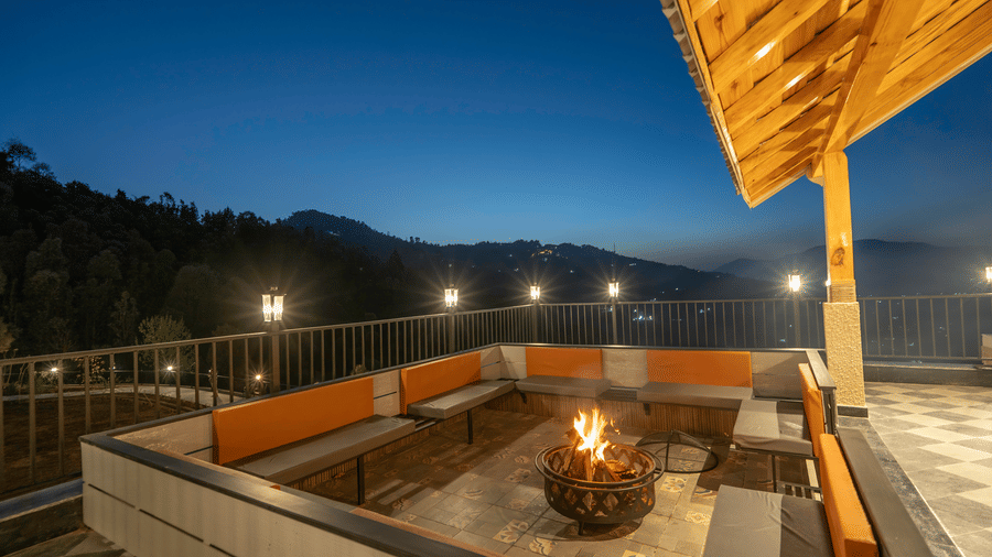 Lit fire in a copper bowl on the terrace at dusk, with cushioned bench seating, lamp posts along the railing and hills beyond at The Chamomile Estate.